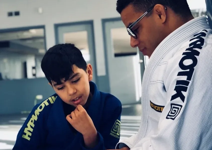 An Apex coach in a white gi working one-on-one with a young student in a blue gi